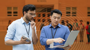 Image of two men wearing Raptor badges reviewing risk and threat assessment on a laptop outside of a school.