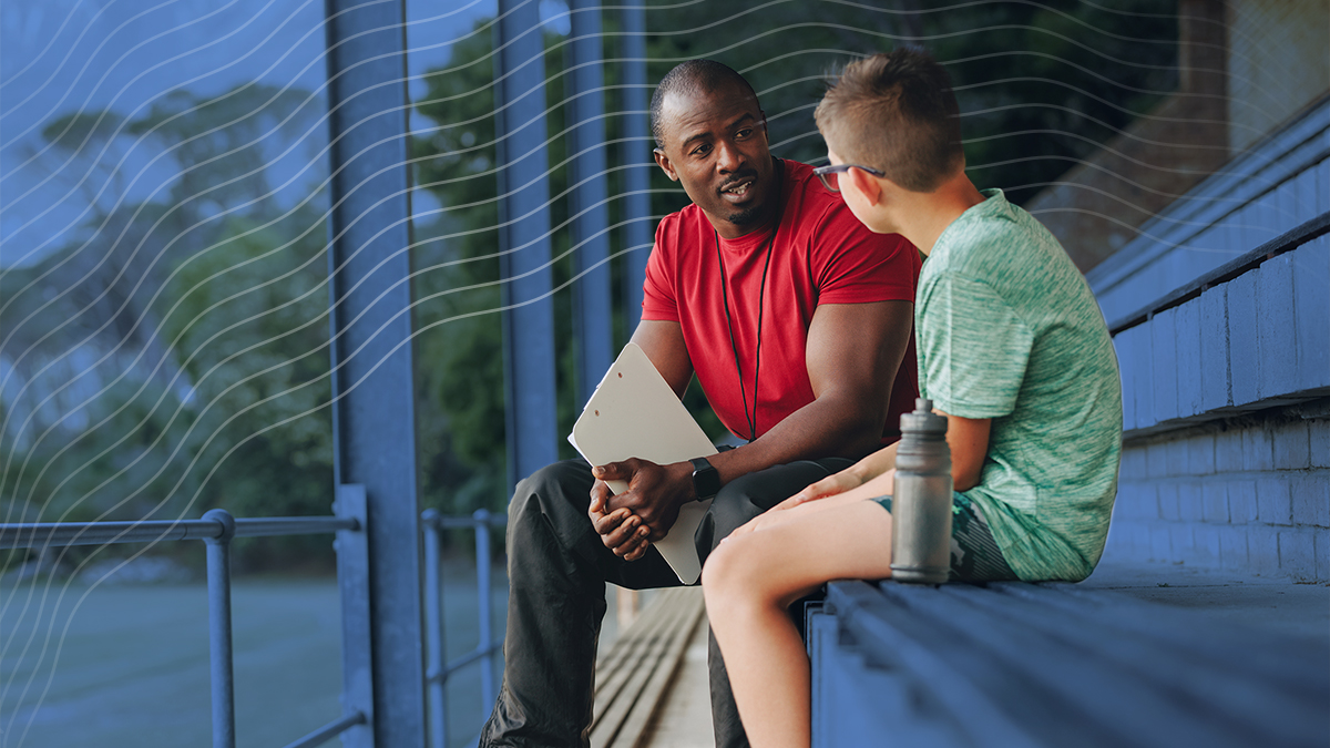 A coach or mentor speaking with a young boy outside on bleachers
