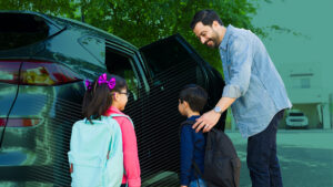 Cheerful father smiling while picking up his young children from elementary school and getting them into the car