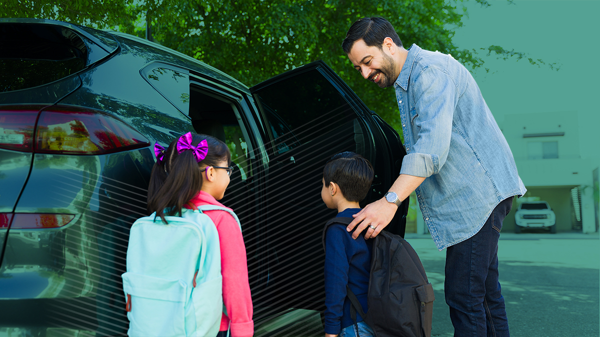 Cheerful father smiling while picking up his young children from elementary school and getting them into the car