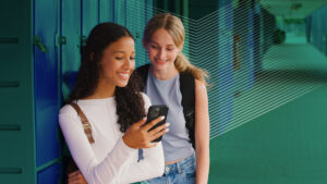 Two teenage girls on hall pass checking their phones at their lockers due to a bell-to-bell cellphone ban