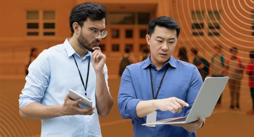 Image of two men wearing Raptor badges reviewing risk and threat assessment on a laptop outside of a school.