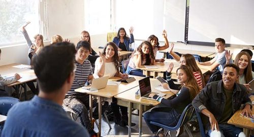 Rear View Of Male High School Teacher Standing At Front Of Class Teaching Lesson