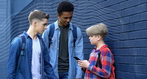 Senior pupils threatening younger boy with phone outside at school